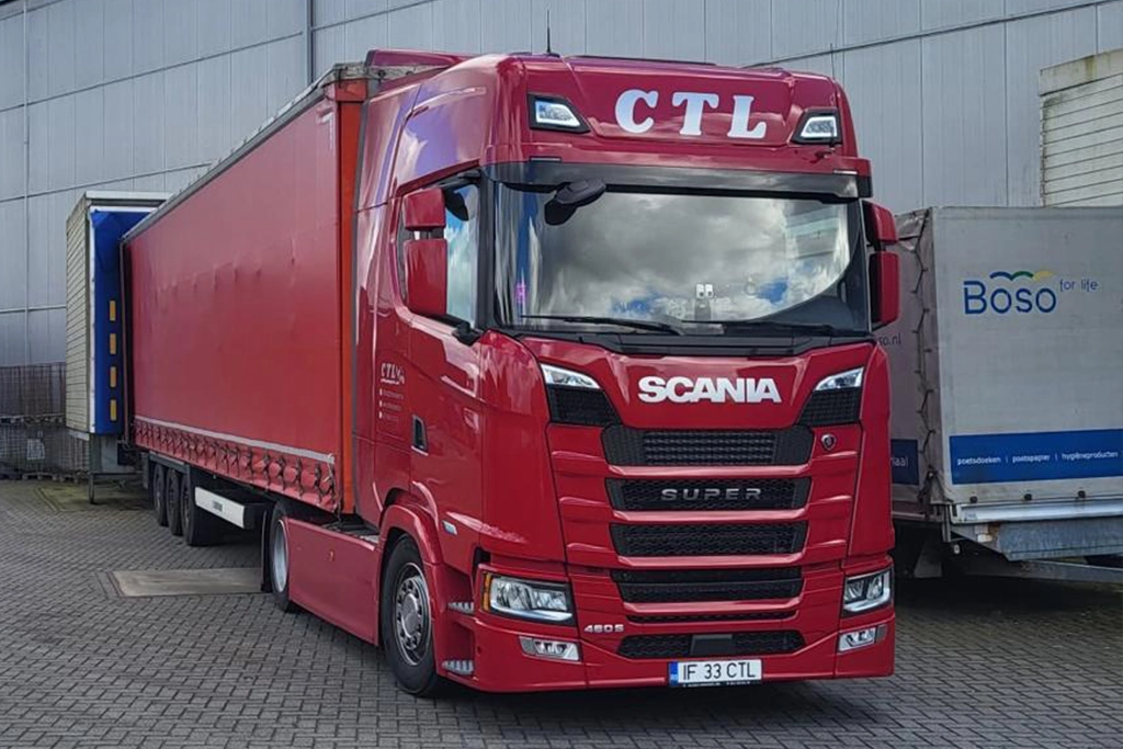Camion Scania rosu si semiremorca cu prelata asteptand in ramp sa incarce